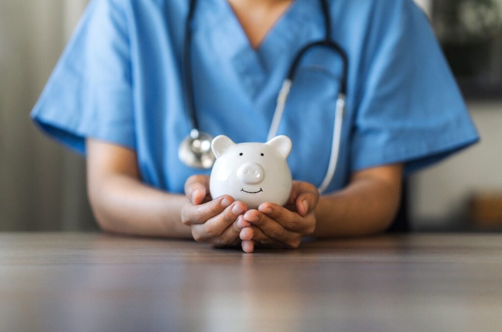 Krankenschwester oder Arzt mit Stethoskop hält ein Sparschwein in der Hand.